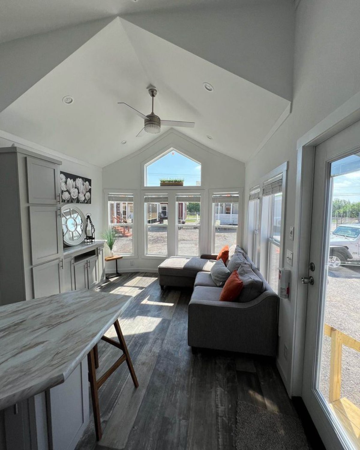 Spacious and bright living area of 399 sf Tiny House has a L shaped couch and wall cabinet with big windows
