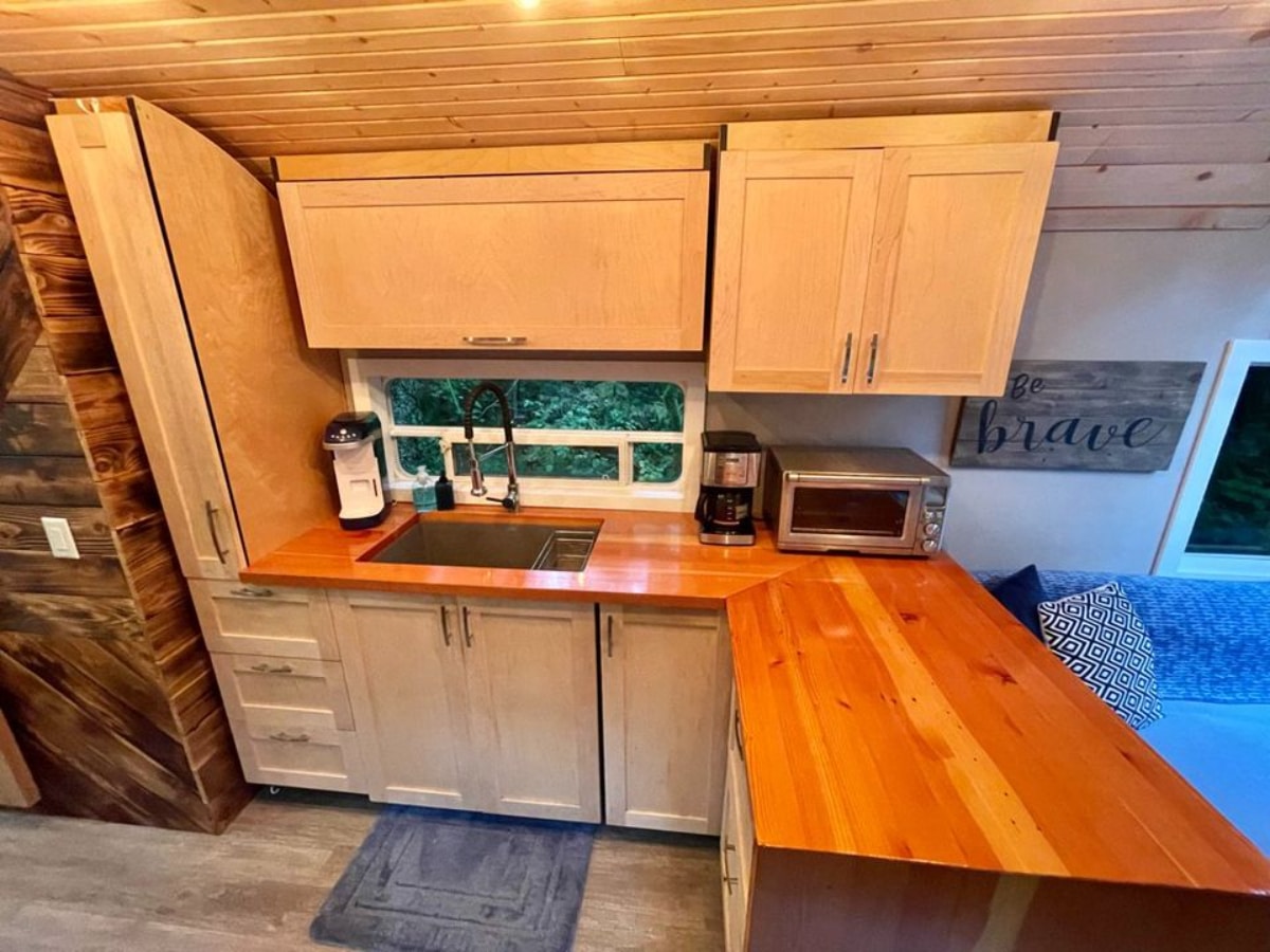 Wooden kitchen area of 40' School Bus Converted Tiny House has a countertop, drawer and a freezer
