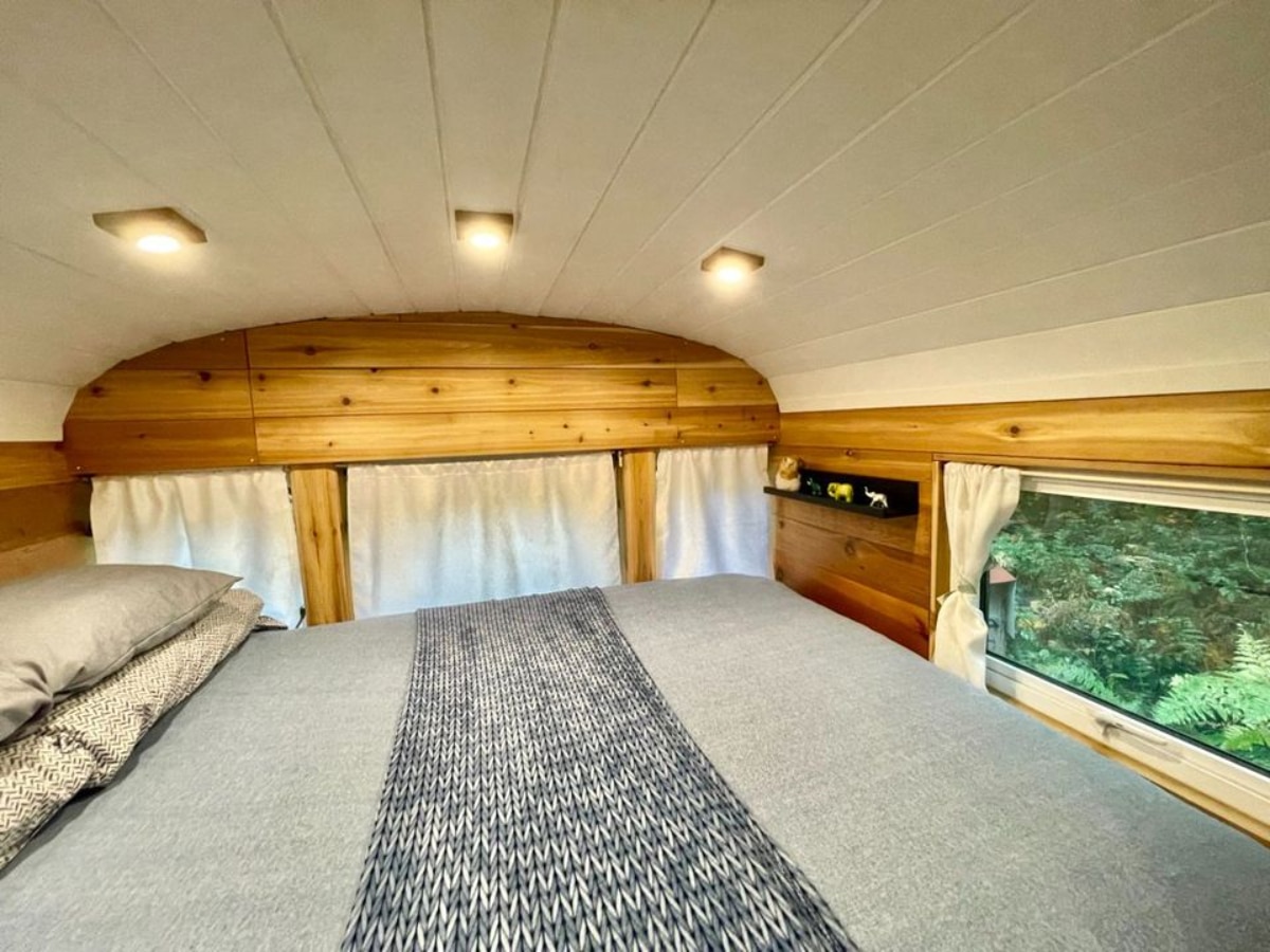 Bedroom of 40' School Bus Converted Tiny House has a queen bed and large windows which makes it brighter
