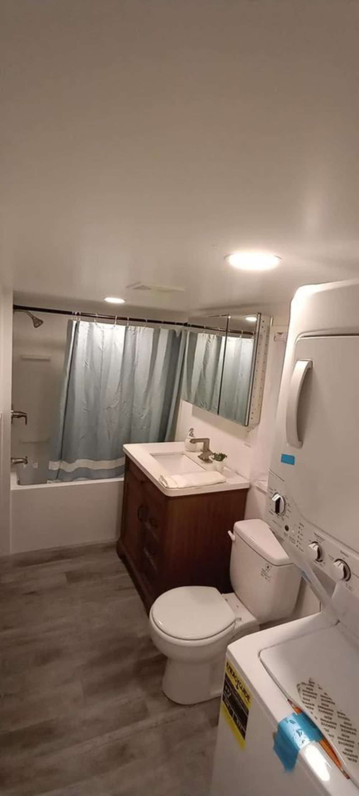 Bathroom of 400 sf Tiny House has washer dryer, standard toilet, sink with vanity and mirror nd bathtub