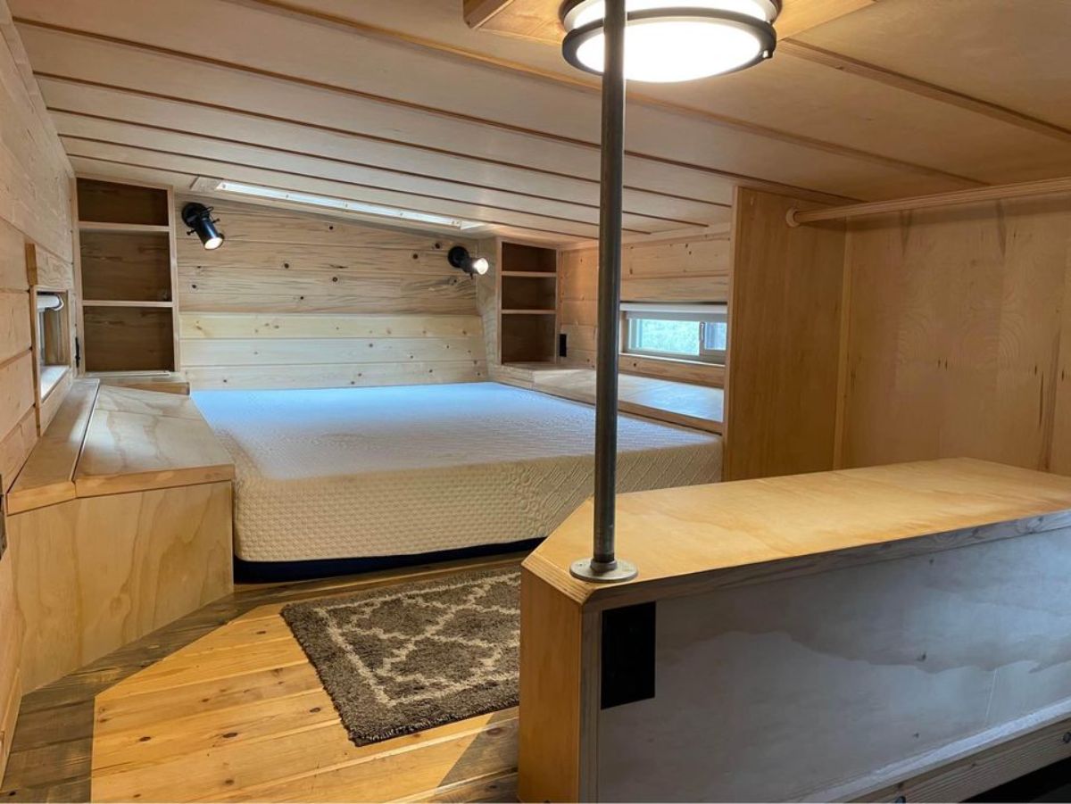 Stunning loft bedroom of 24’ Rustic Tiny House On Wheels has queen mattress, book shelf and addition ample space