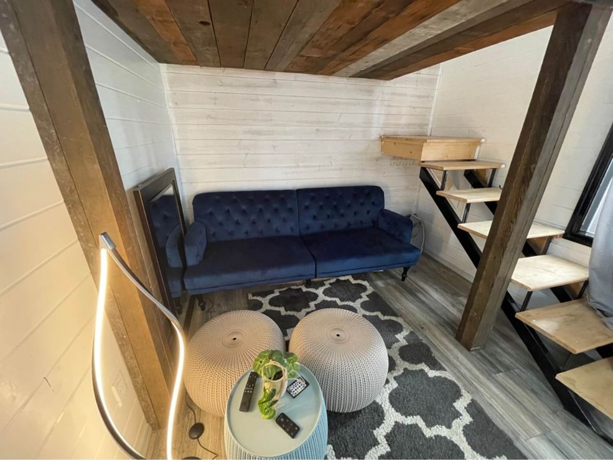 Living area of 24’ Turnkey Ready Tiny House has a couch and there is a stairs towards the loft