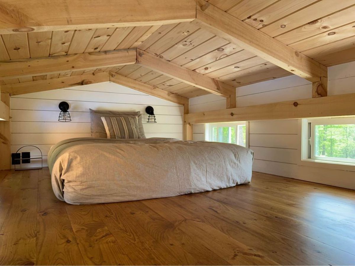 Gorgeous and very spacious bedroom of 26’ Timber Framed Tiny House has a queen mattress, few wall hangings and still ample space