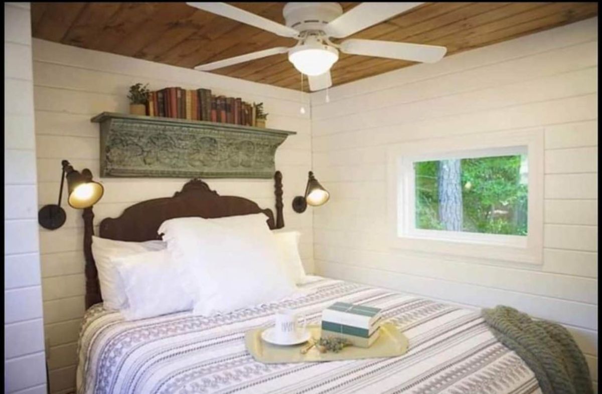 Bedroom of 450 sf Tiny Home has a comfortable bed, side tables, few shelves above the bed and a window
