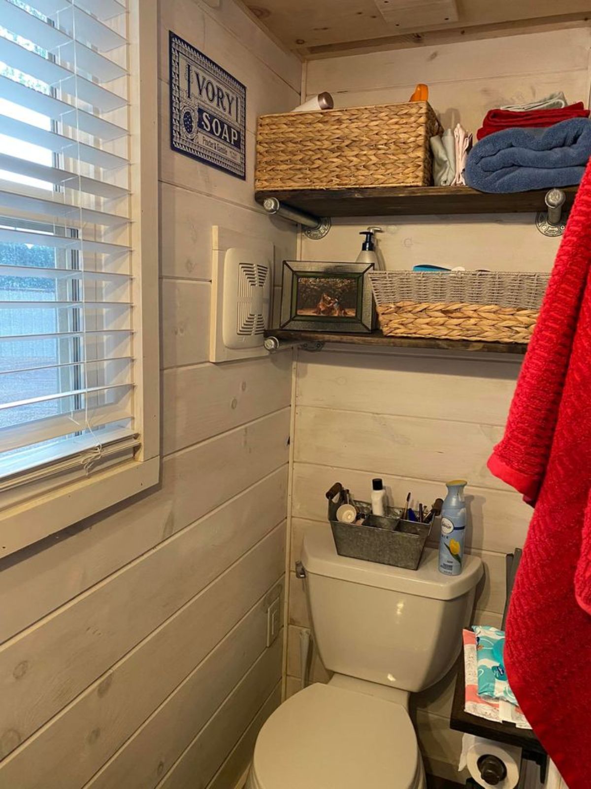 Bathroom of 198 sf Tiny Cottage has a standard toilet, shower area and open shelves for all the toiletries