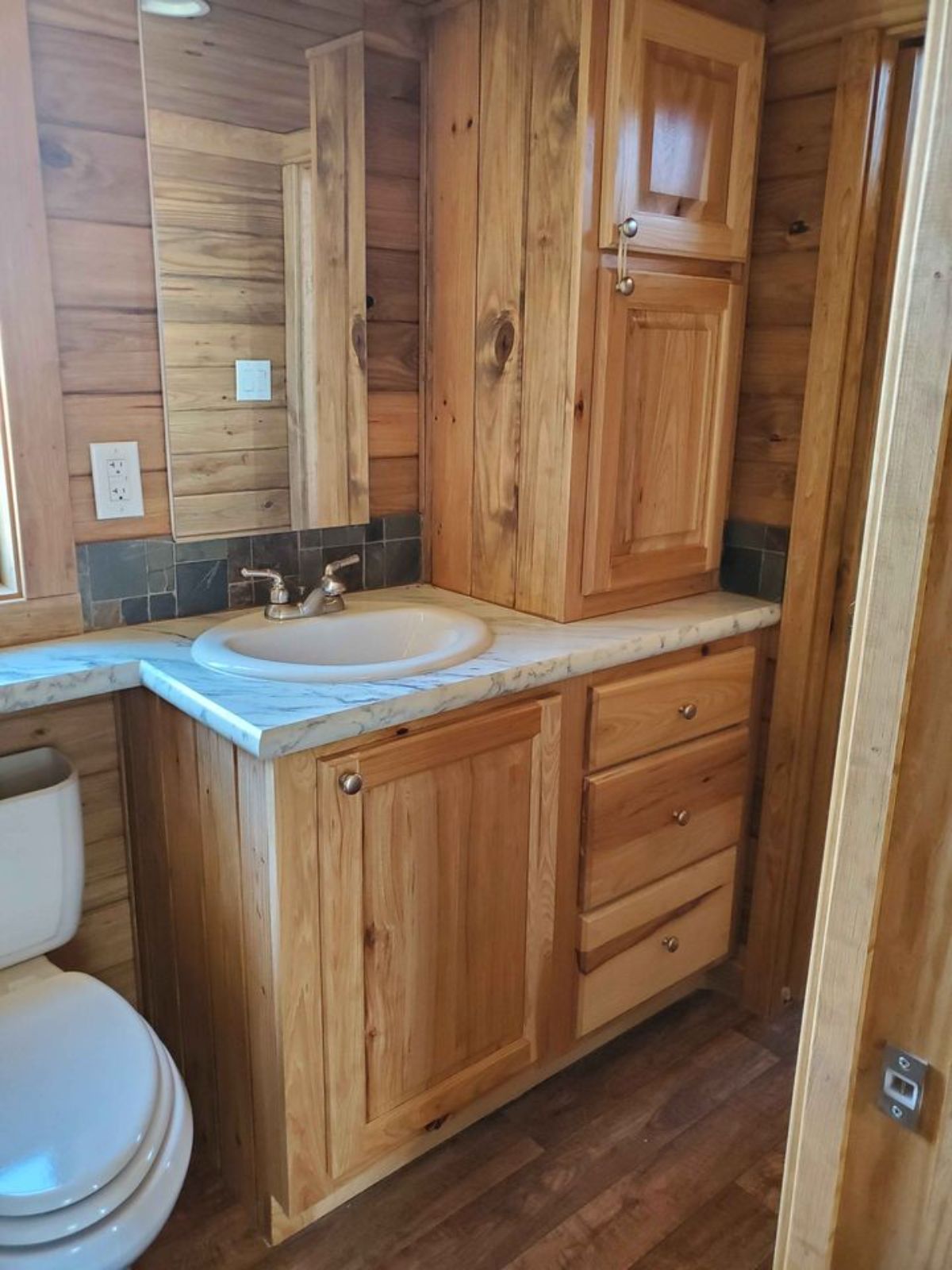 Standard toilet and sink with vanity and mirror along with Wooden storage in bathroom of 399 sf Park Model Tiny House