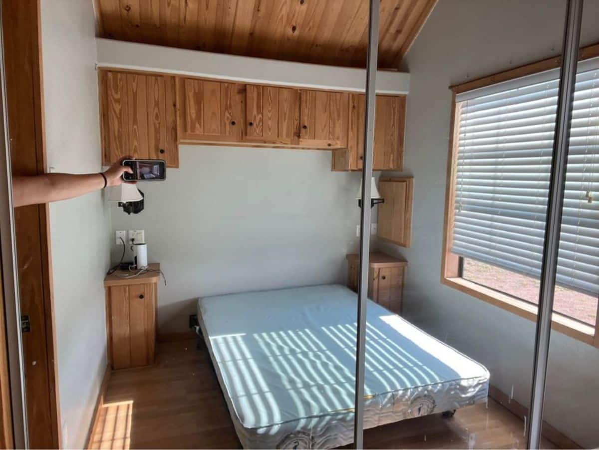 Main floor bedroom of 40’ Tiny Home has a queen bed, side tables, wall mounted storage and wardrobe with mirror