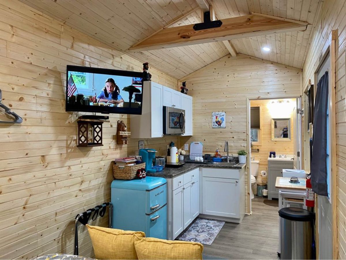Furnished kitchen area of 24’ Tiny Home Shell on Wheels has wall mounted television set facing the living area