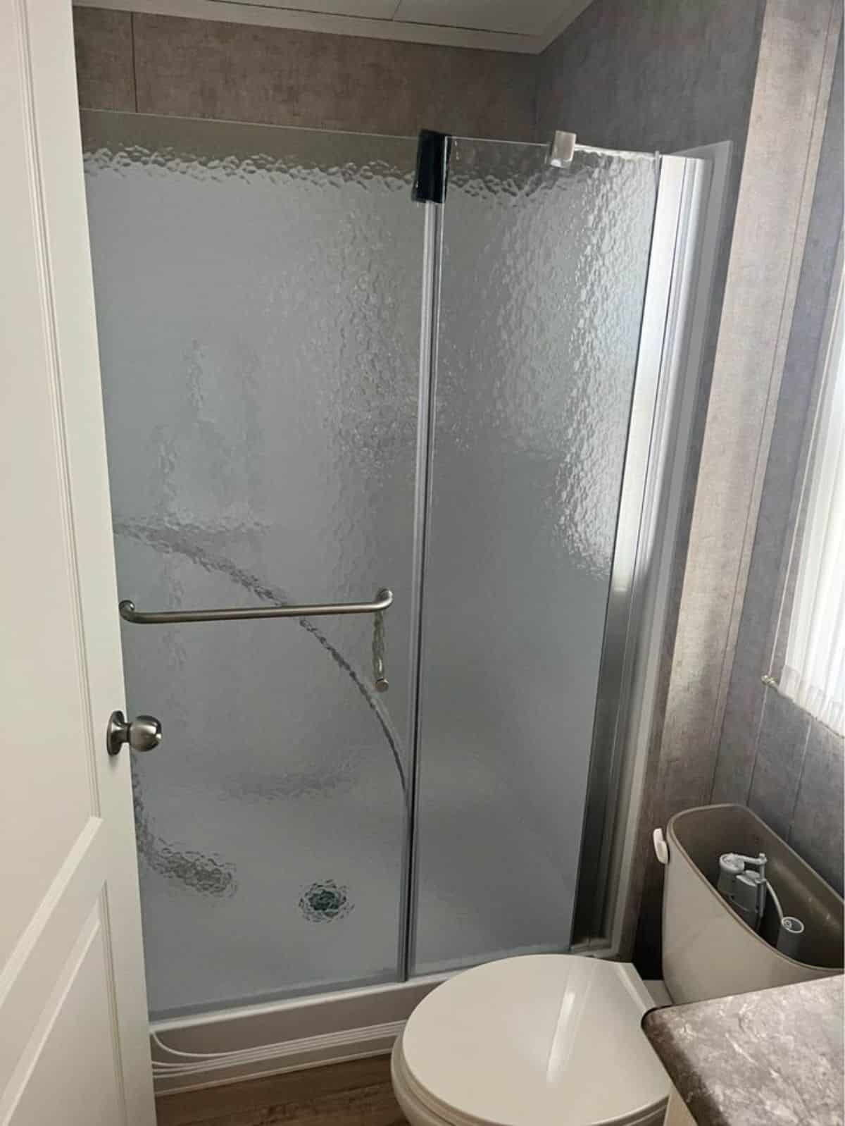 Standard toilet and separate shower area with glass door in bathroom