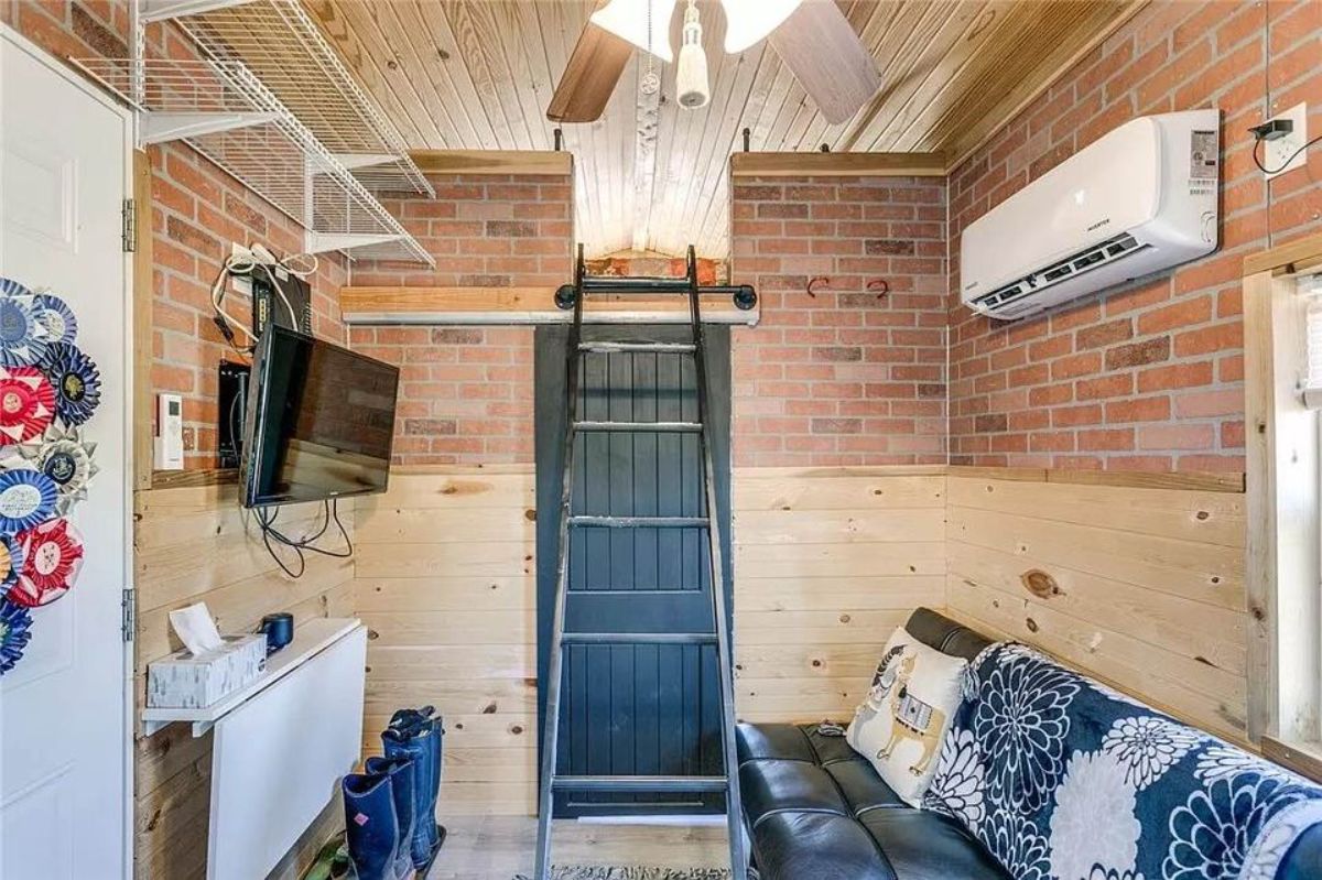 Living area of Adorable Tiny House with Land has a couch, wall mounted television set and an air condition unit
