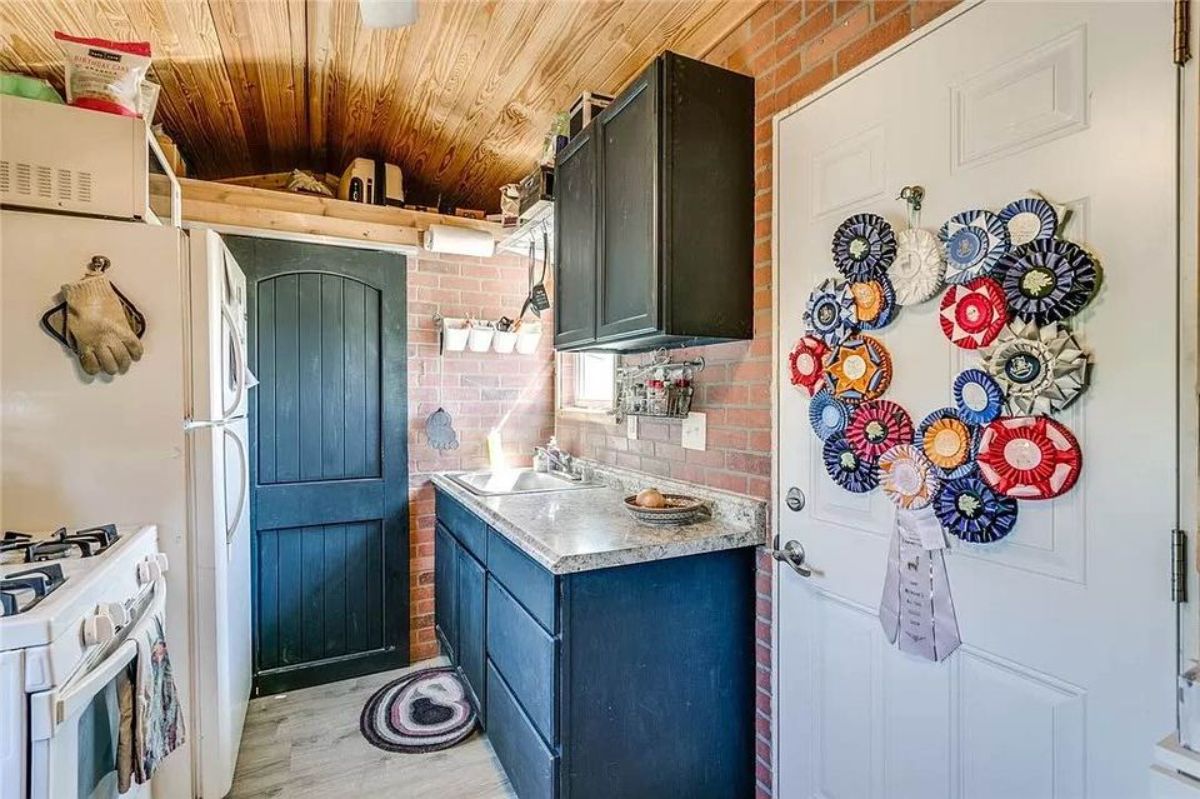 Kitchen area of Adorable Tiny House with Land has a refrigerator, 4 burner gas oven