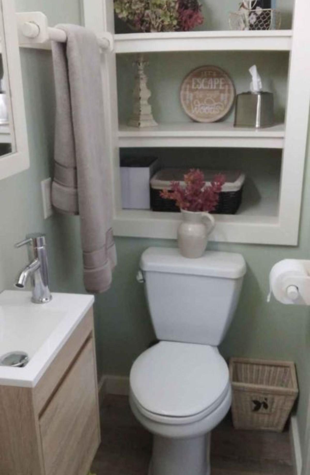 Standard toilet, sink with vanity & mirror in bathroom and little storage of 2 Bedroom Tiny House