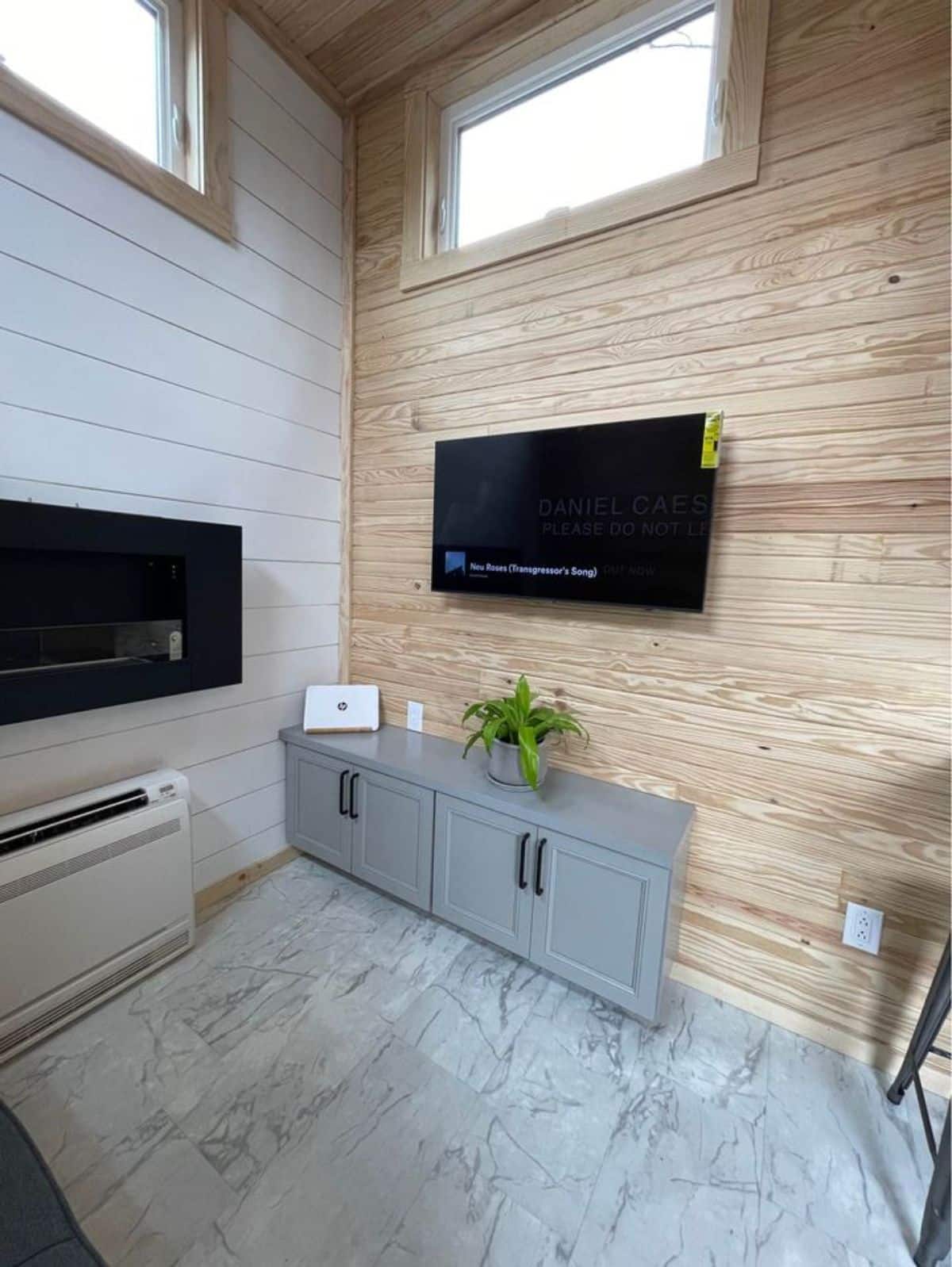 Opposite to the couch there is wall mounted television set with small wooden storage table