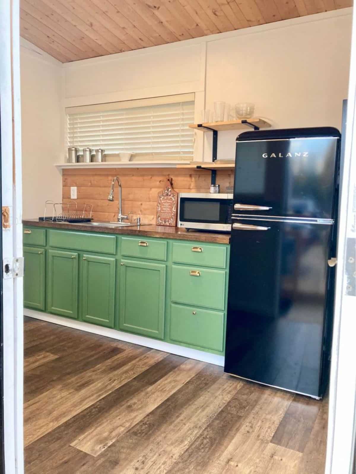 Kitchen area of 25' Beautiful Tiny Home  has refrigerator, microwave oven, counter top, sink and storages