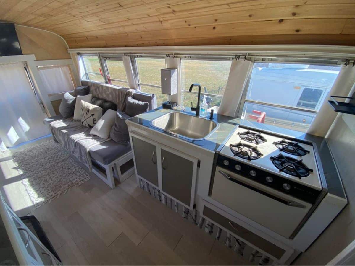 Stainless steel single basin sink, propane gas range and oven in kitchen area of Classy wooden interior of 40' Skoolie Tiny House on wheels