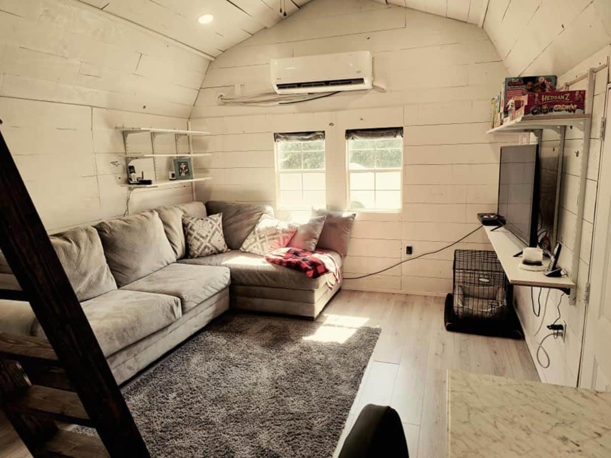 Living area of 40' Tiny House with Main Floor Bedroom has a L shaped couch with wall mounted TV set
