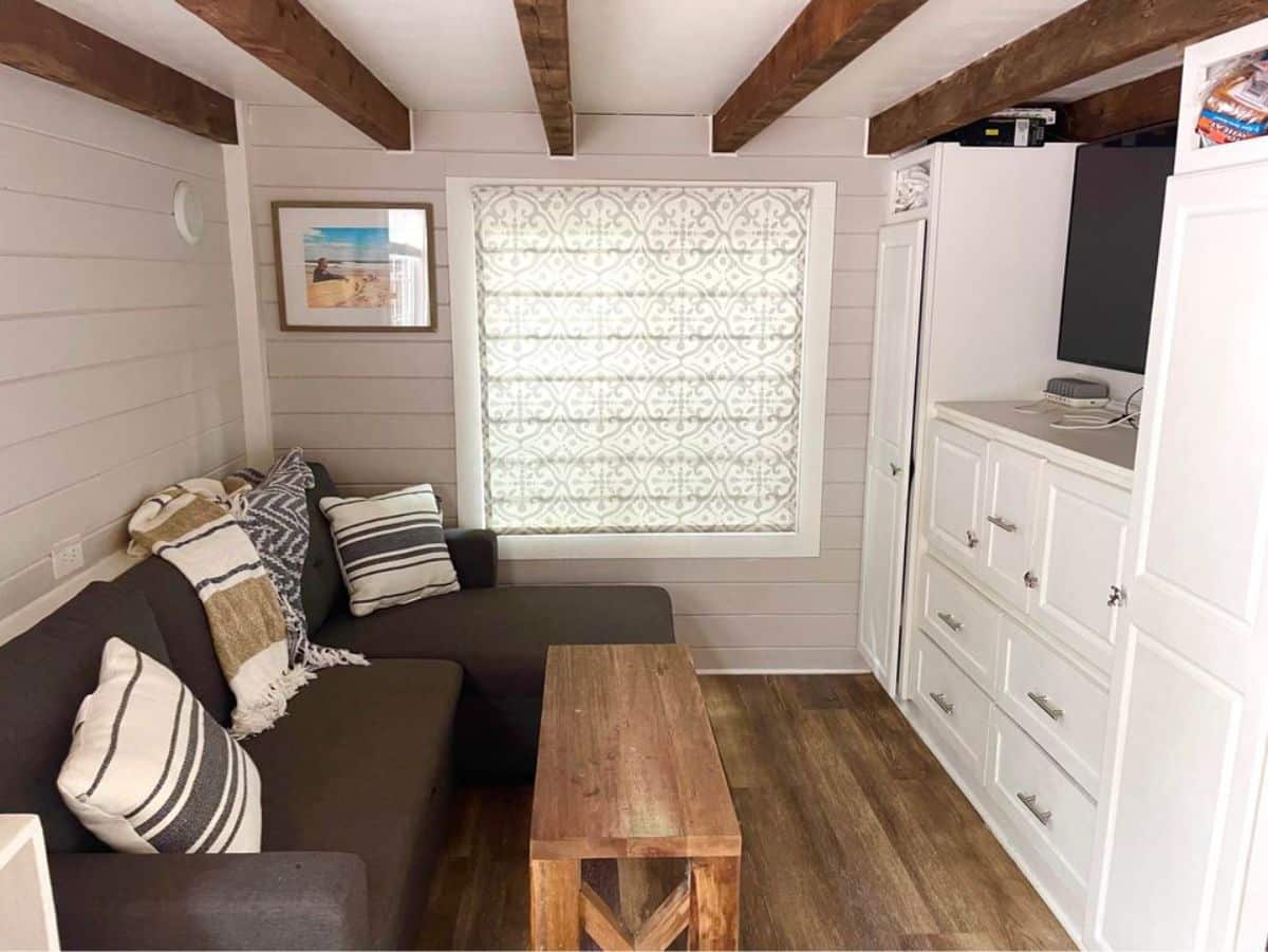 Living area of Stunning 3 Bedroom Tiny House has a couch, center table, wall mounted television set with entertainment center.
