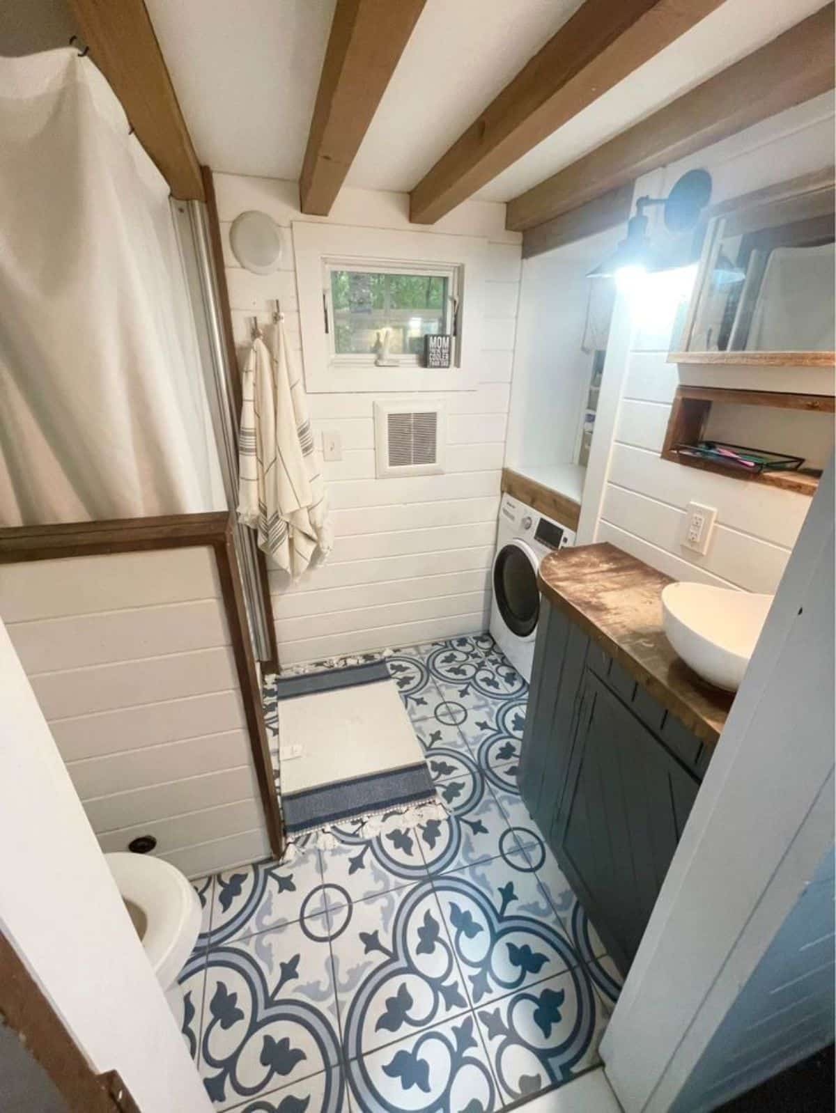Bathroom area of Stunning 3 Bedroom Tiny House has sink with vanity & mirror, standard toilet, separate shower area, washer dryer combo and lots of storage.