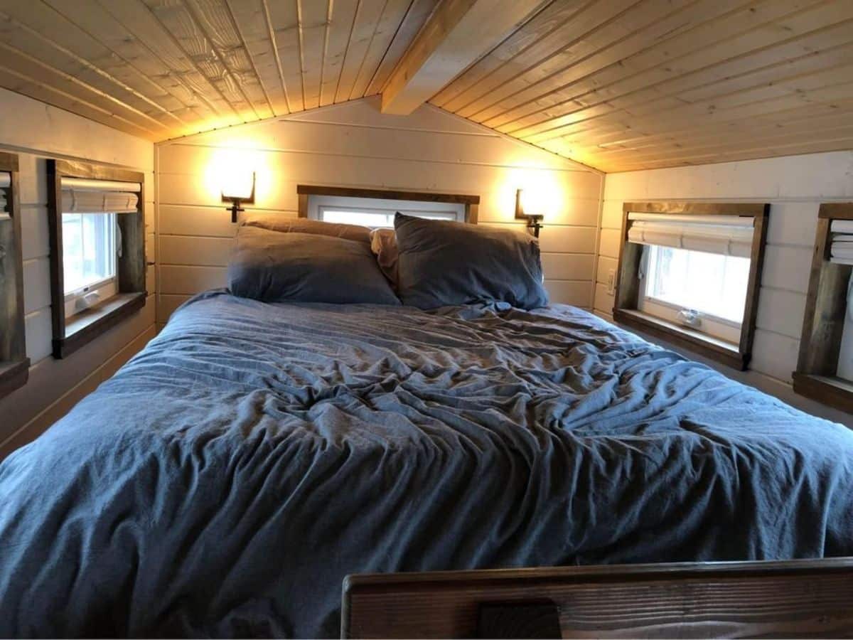 Huge loft bedroom has a cozy queen mattress with lamps and windows