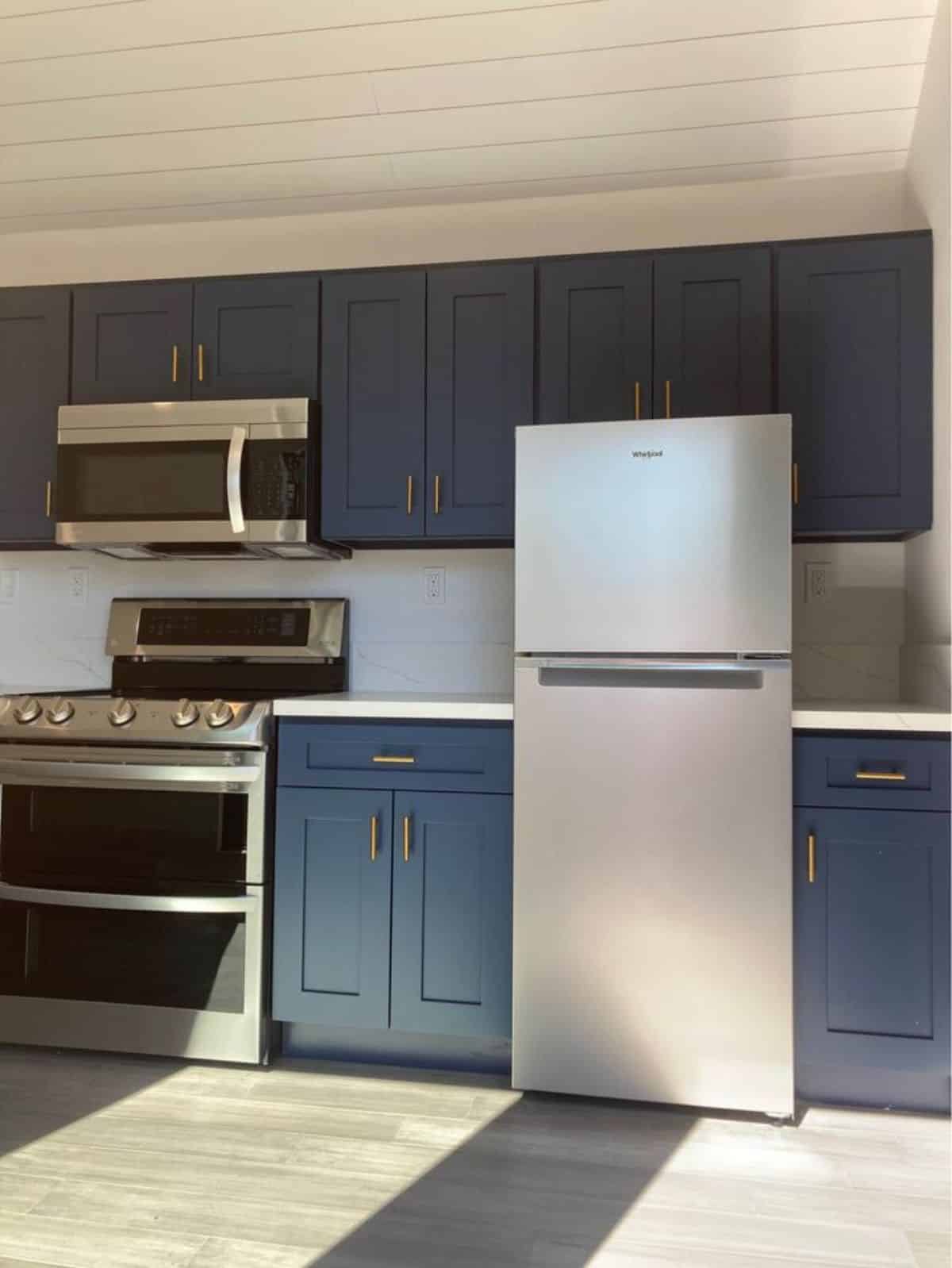 Blue colored kohler kitchen looks stunning with full length refrigerator, microwave oven cum burner and storage