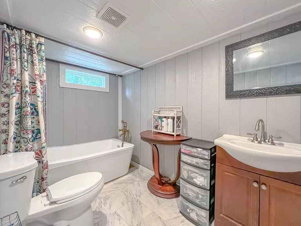 Common bathroom has a bathtub, standard toilet, sink with vanity & mirror and racks