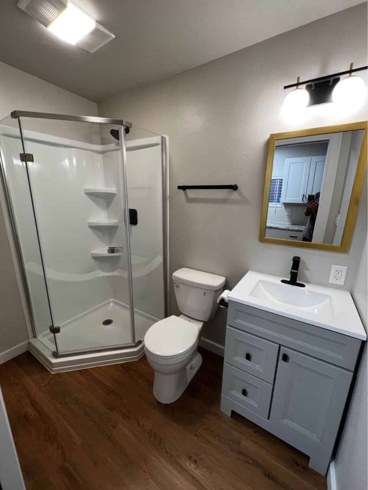 Bathroom of Brand-New Tiny Home has a standard toilet, sink with vanity & mirror and glass door separate shower area
