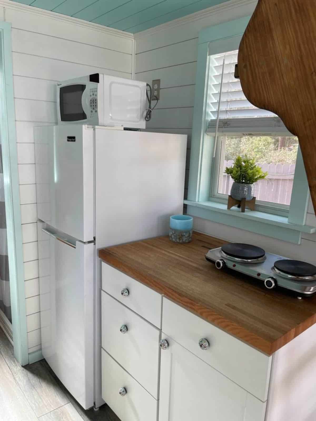 Refrigerator, microwave, and a 2-burner cooktop with storage cabinets on the other side