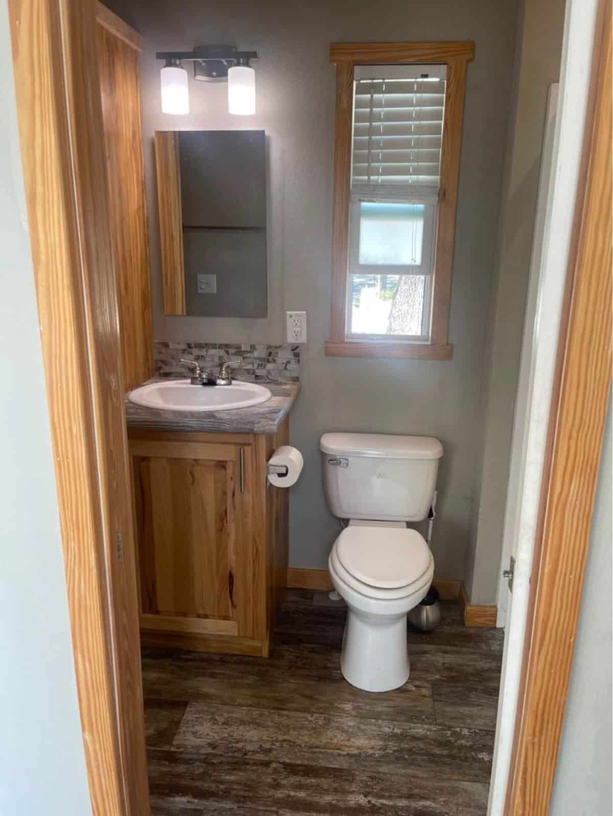 Well organized bathroom of Park Model Tiny Home has a standard toilet, sink with vanity & mirror and shower