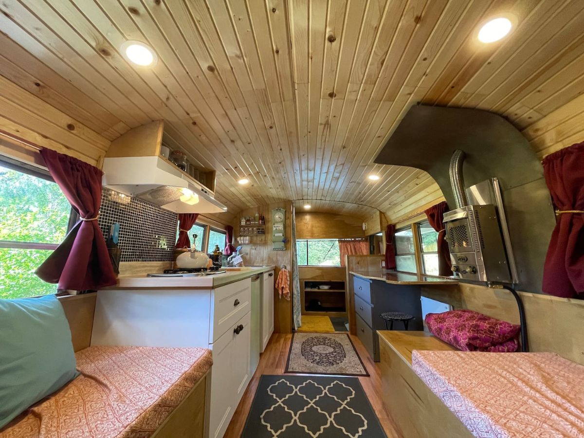 gray and white rug in center aisle of bus with seat on right and kitchen counter on left