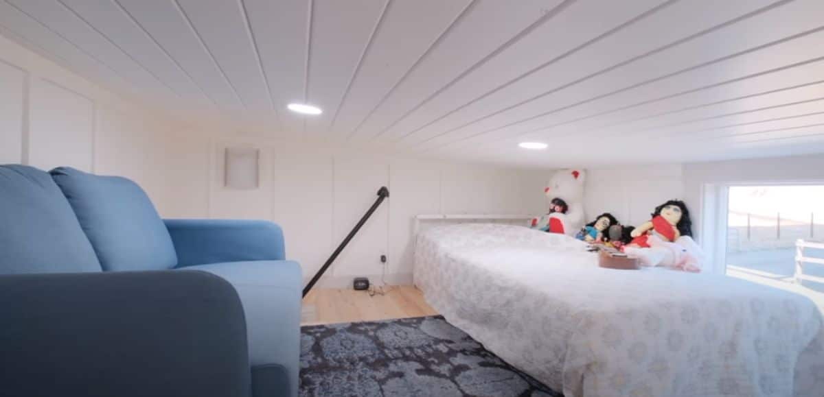 white bed on right and blue sofa on left of loft