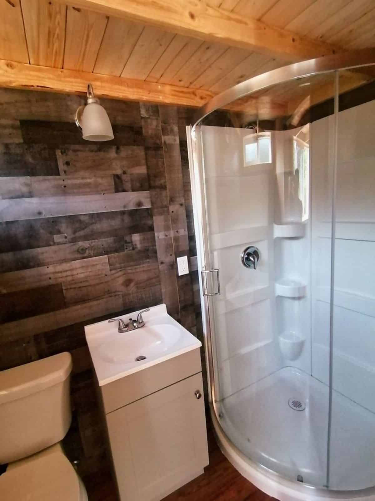 Standard toilet, sink with vanity and separate glass door shower in bathroom of Cozy Tiny Home