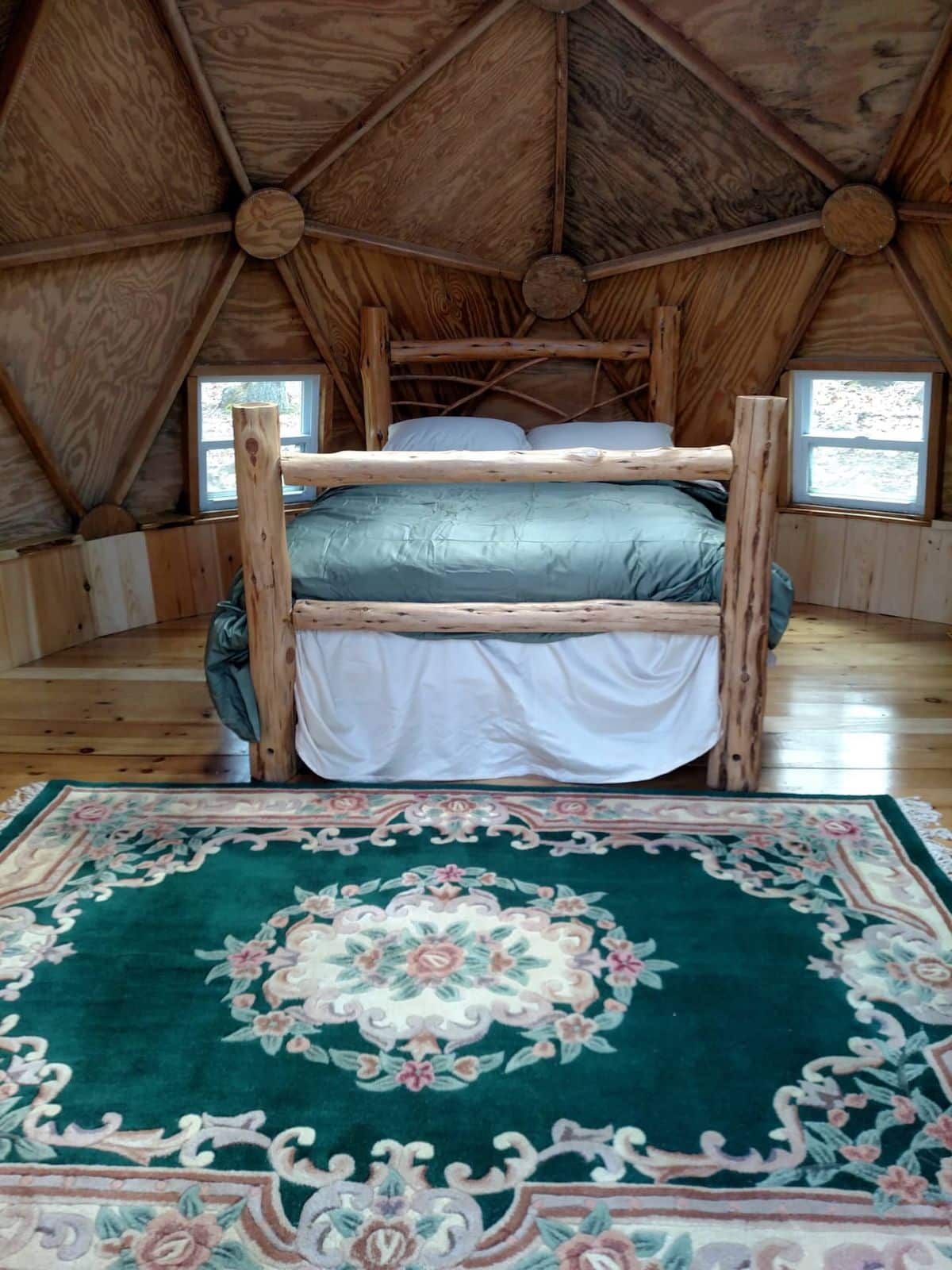 green floral rug in front of wood bed inside wood dome
