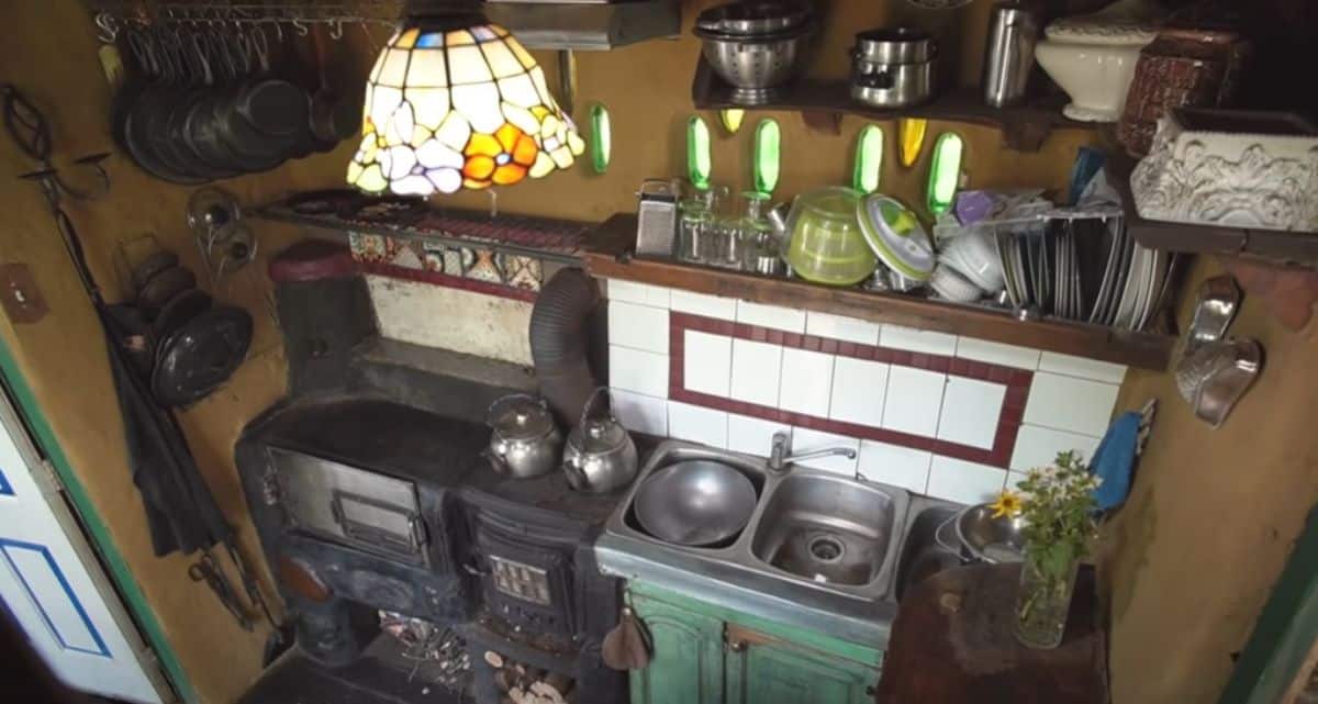 green cabinets below stianless steel sink with old fashioned wood stove