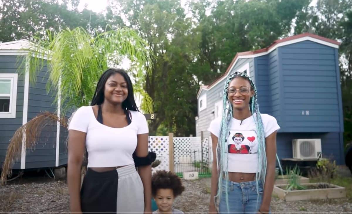 two black woman and a small child standing in front of tiny houses