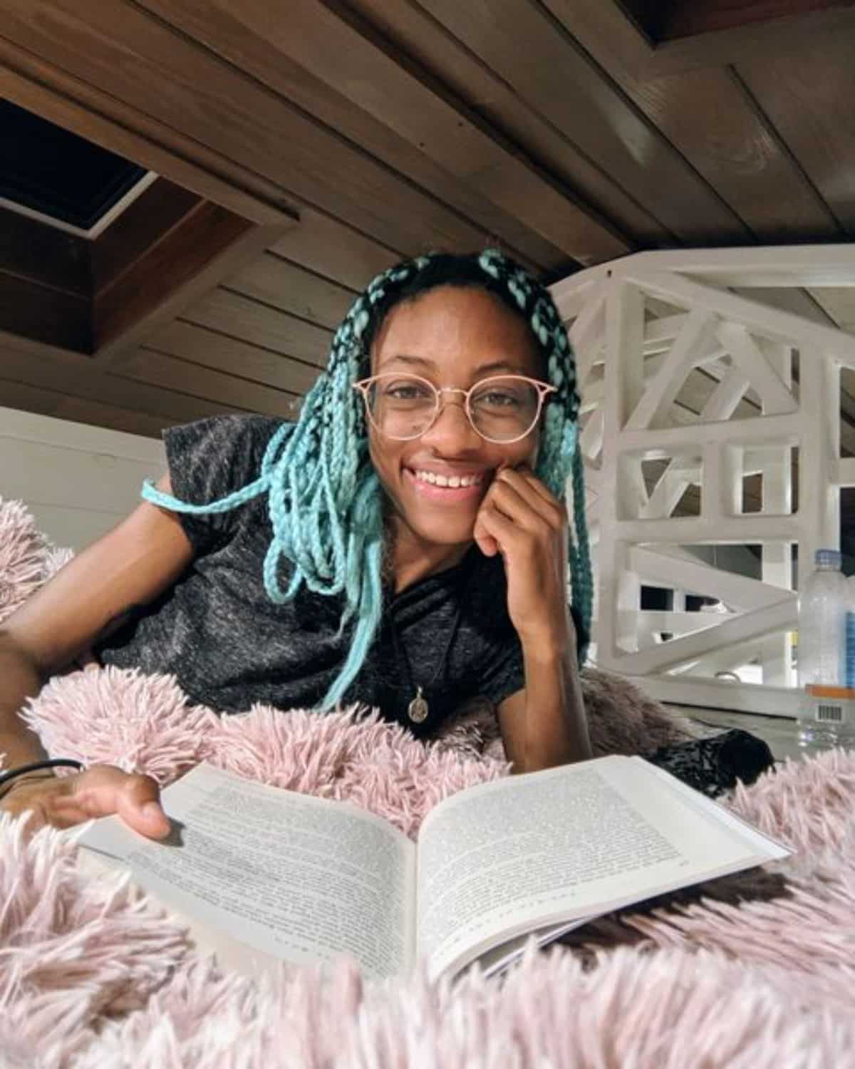 woman with blue braids on bed with book