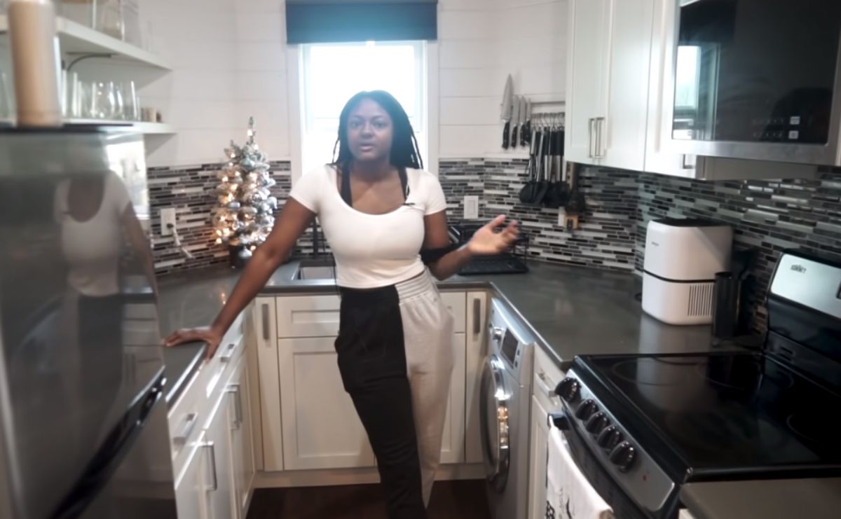 woman in white and black pans in tiny kitchen with dark tile and countertops