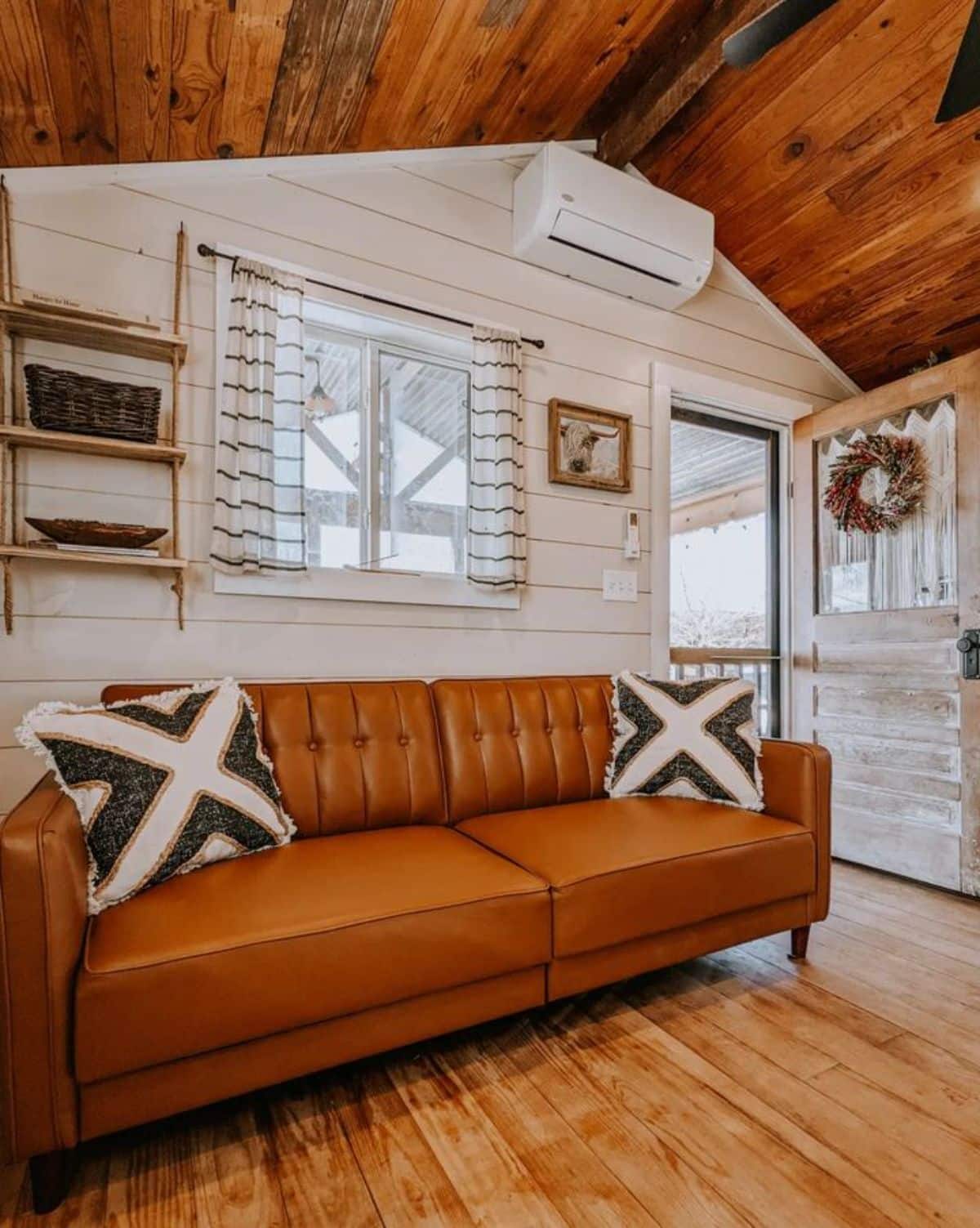 brown leather sofa against white wall near open door to tiny home