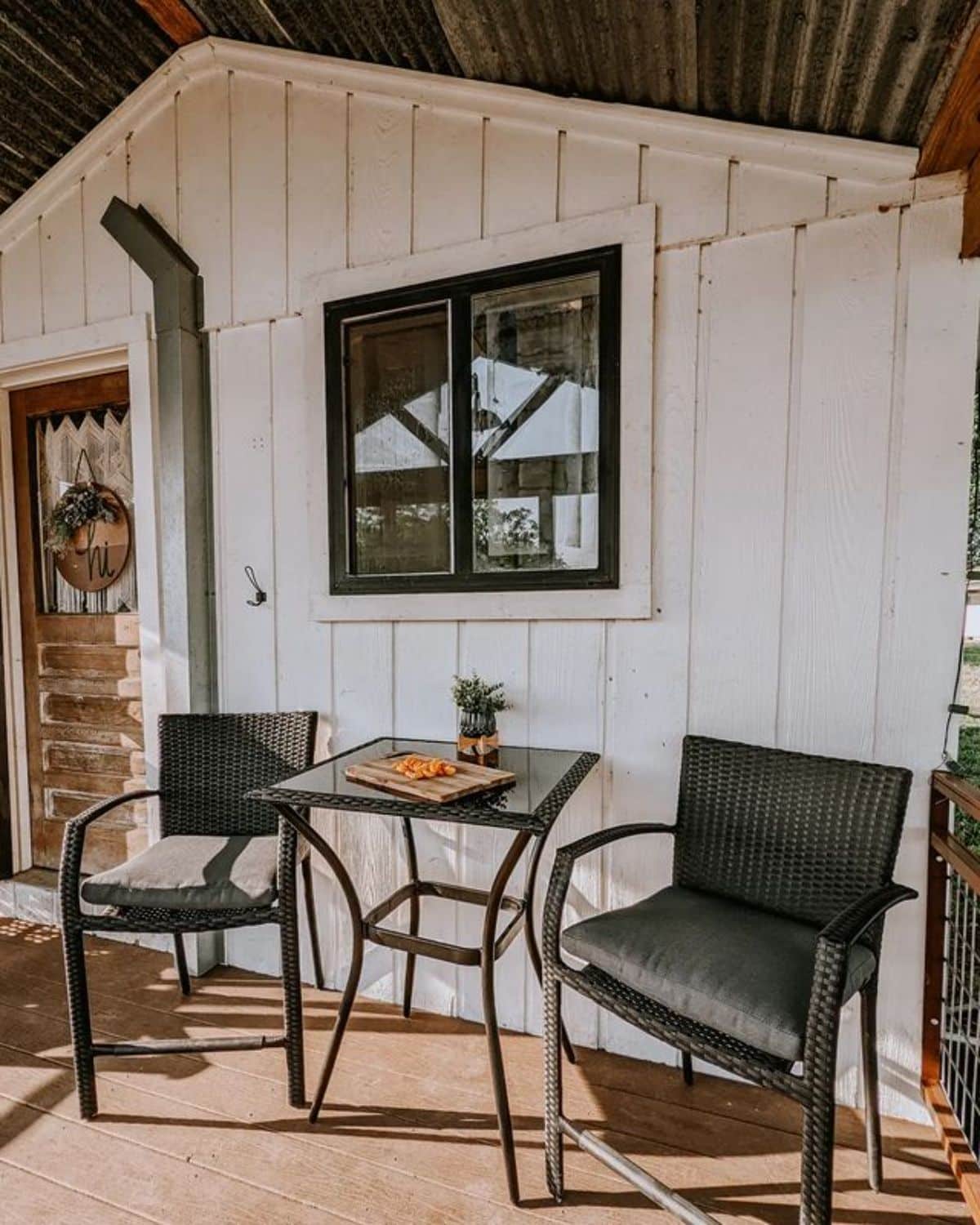 white siding on tiny house with black chairs and table on porch