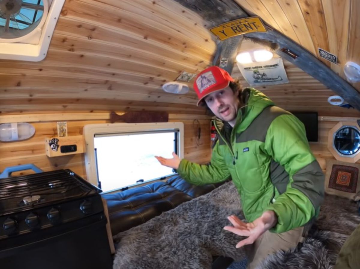man in green jacket showing how to fold down futon bed inside tiny house truck