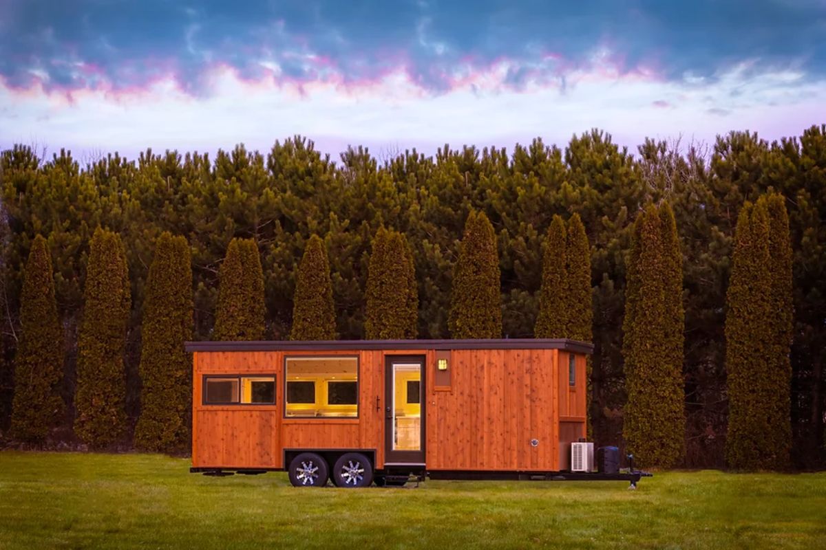 wood siding, black trim, tiny house on wheels, trees in background