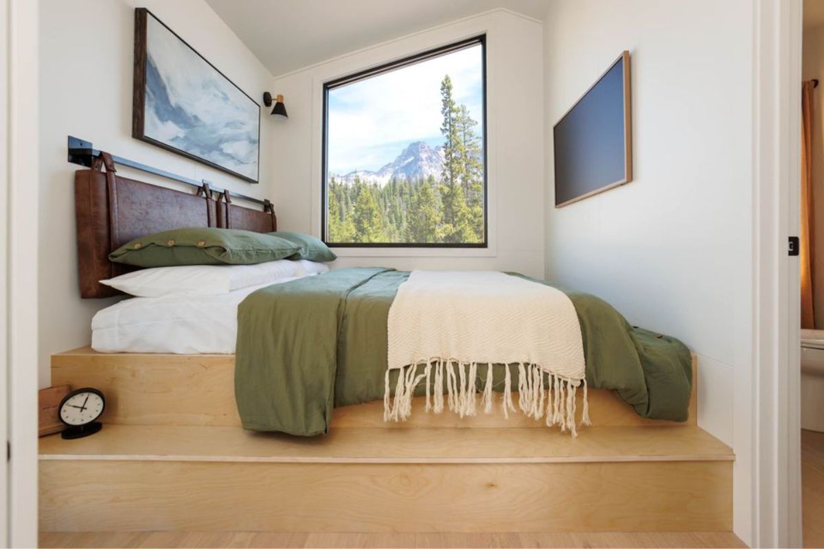 Stylish bedroom of A-frame tiny home has a huge window and comfortable bed