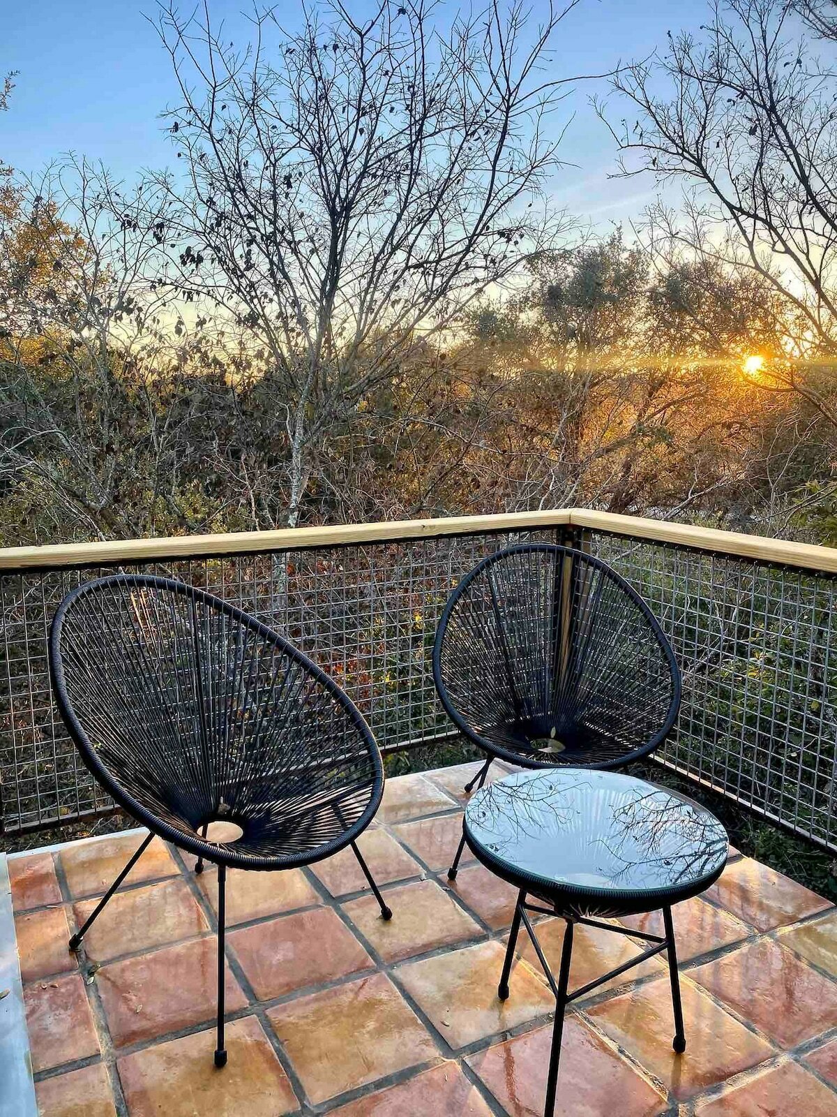 An upper deck seating area with gorgeous views, featuring modern chairs and a small table, heavy wire large square mesh railing panels and large terracotta deck tiles.