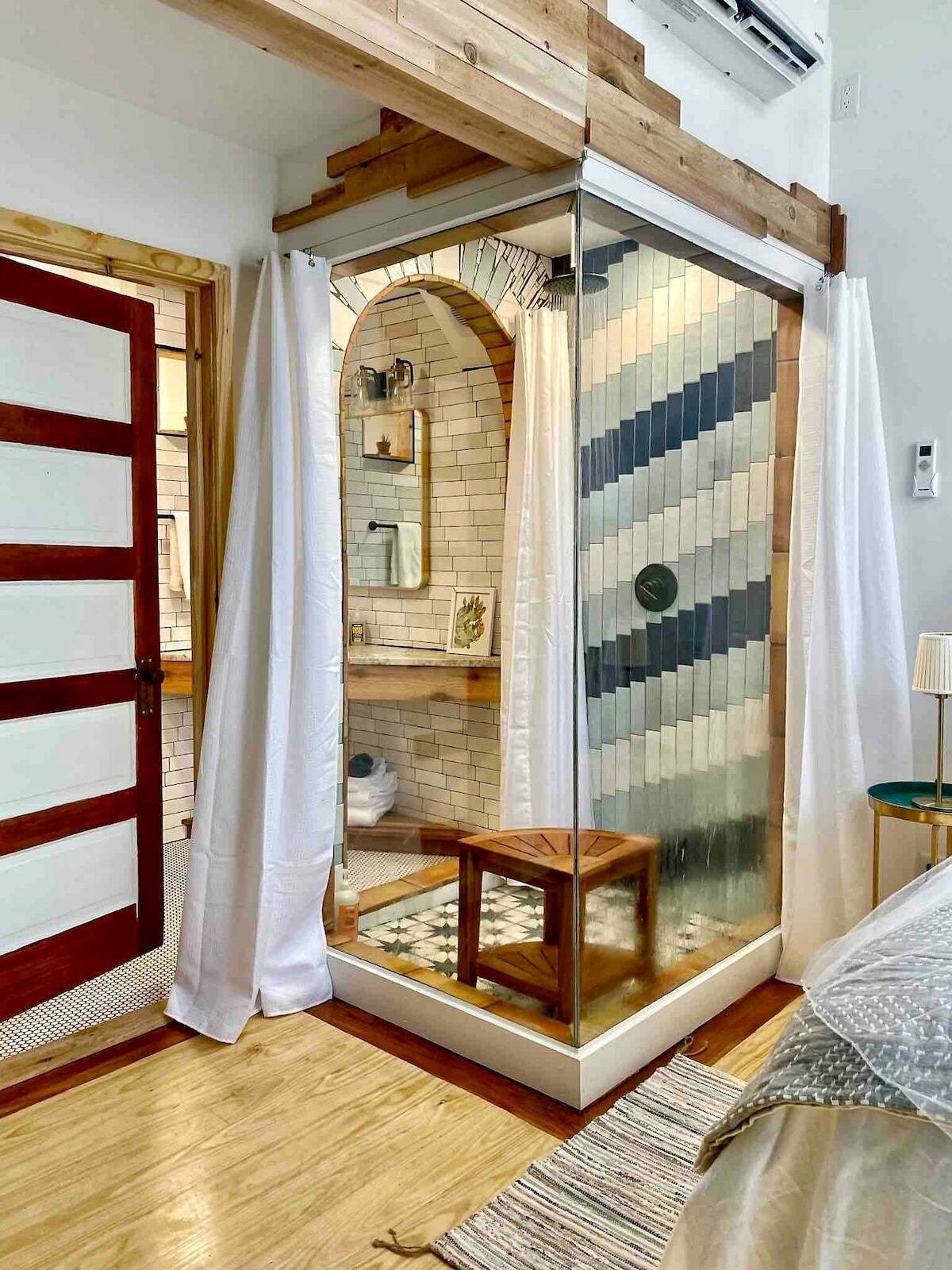 A square shower stall that juts back out into the sleeping area from an artisanally hand-crafted tiled arched entry along the bathroom wall