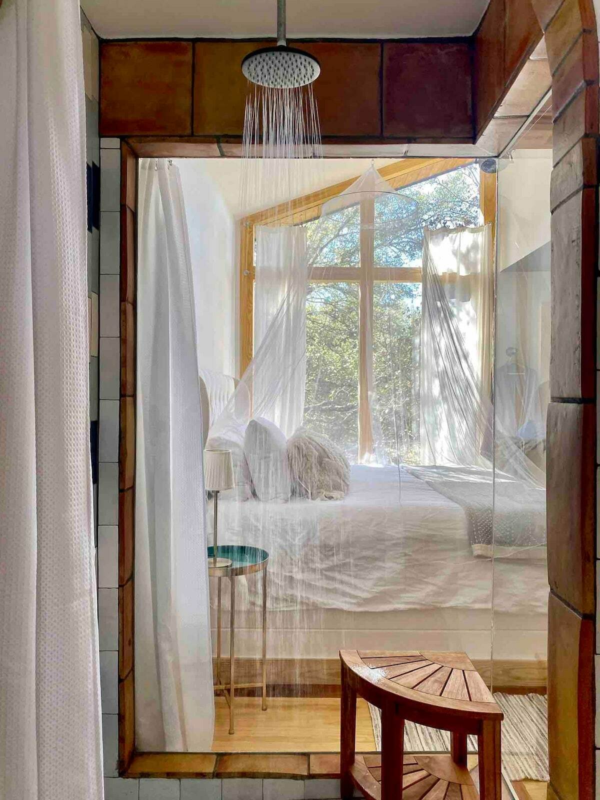 A shower stall view towards the bed, with a rain shower head and a curtain that can be drawn on the bathroom archway to keep water inside of the shower.