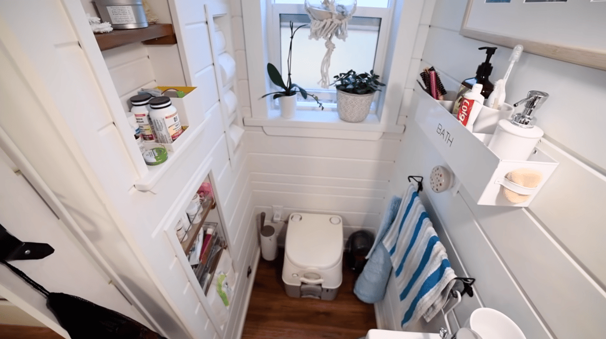 Bathroom with toilet side featuring composting toilet, wall mounted organizer for handsoap, lotion, toothbrush, and toothpaste, and inset shelves on opposite wall