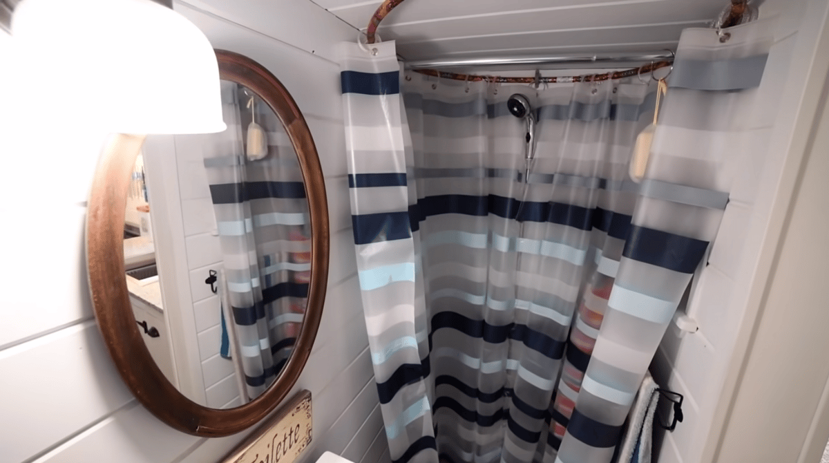 Bathroom with shower side featuring oval mirror over sink and copper piping circle as curtain rod for shower curtains