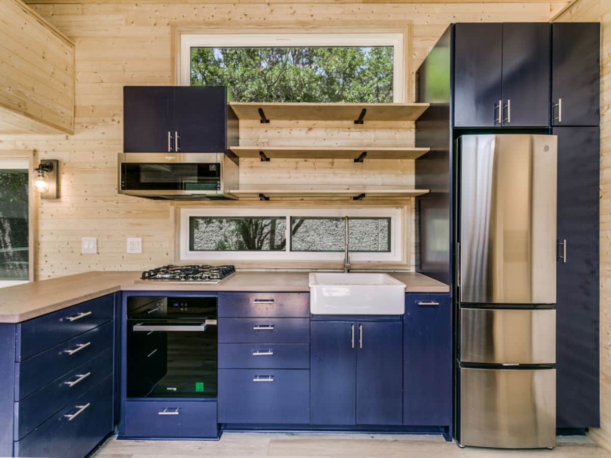 blue kitchen counters in l-shape with black stove and stainless steel refrigerator on right