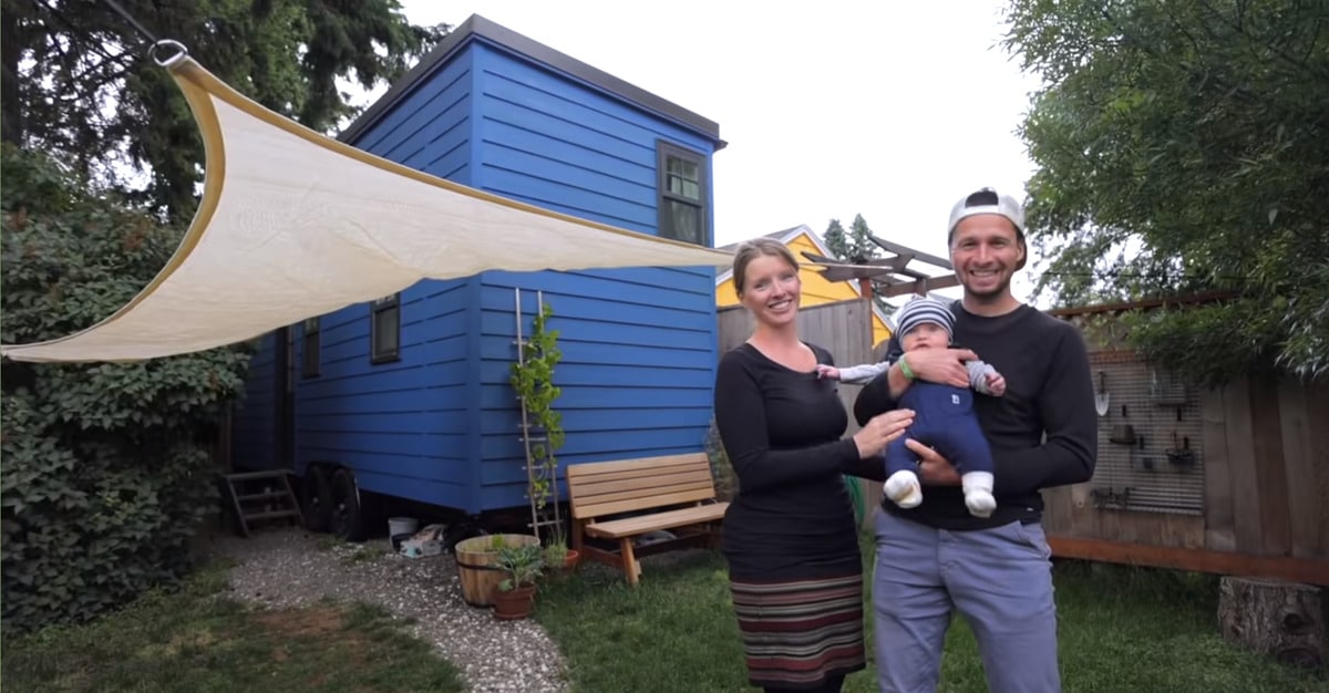 A family poses in front of their 26-foot double-decker tiny house trailer on a sunny day.