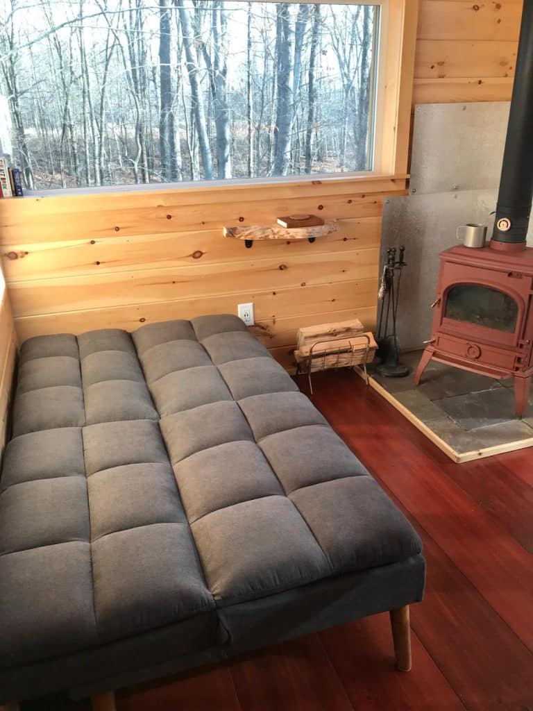 futon bed folded down in front of red and black wood stove