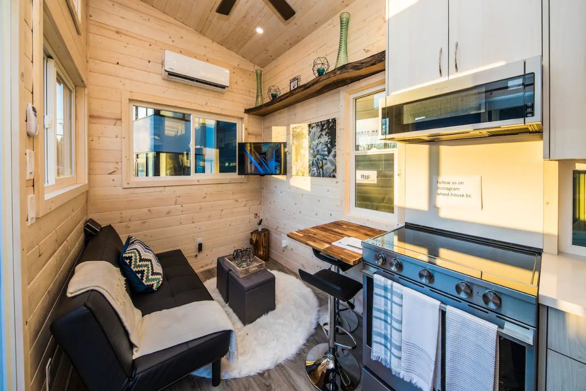 sofa on left with stove on right inside tiny home with light wood walls
